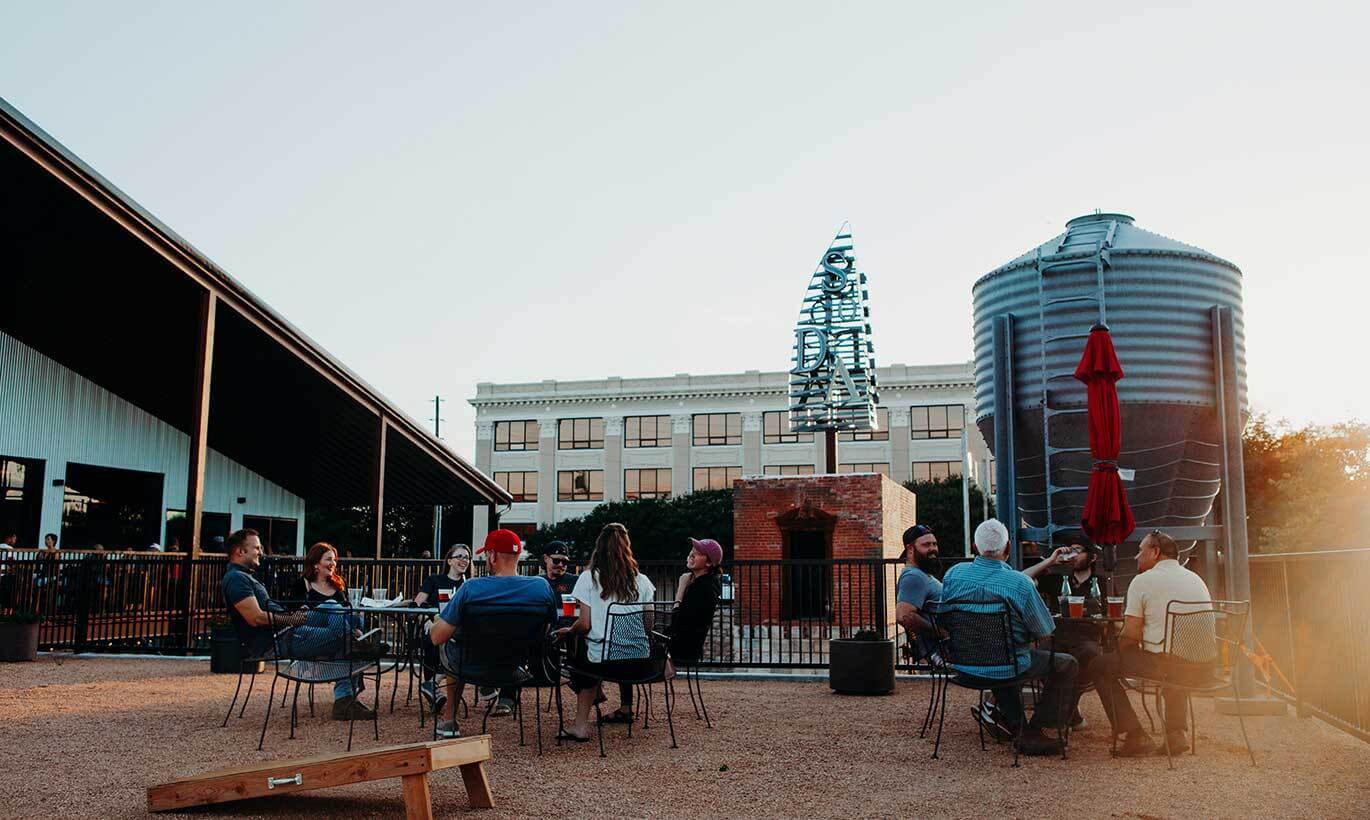 Two groups of people sitting outside enjoying beers at Sockdolager Brewing Co. in Abilene, Texas