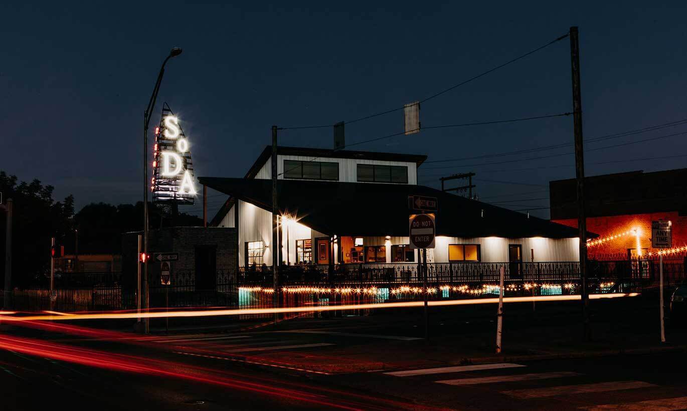 The Sockdolager Brewing Co. building lit up at night by yellow and orange lights inside the building