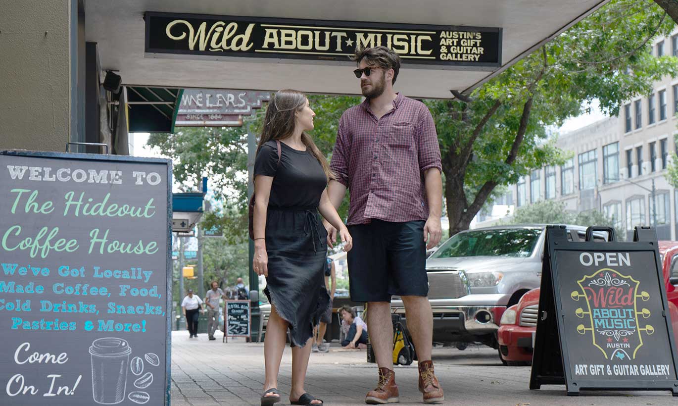 A man and woman walk down the sidewalk in front of a coffeeshop in Austin, Texas.