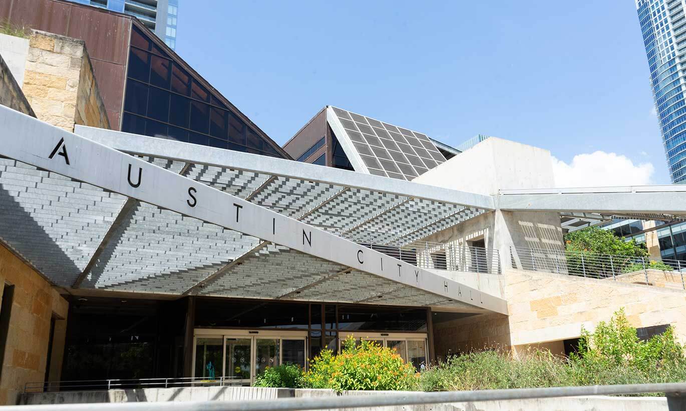 The geometric Austin City Hall sits amongst other corporate buildings in downtown Austin, Texas.