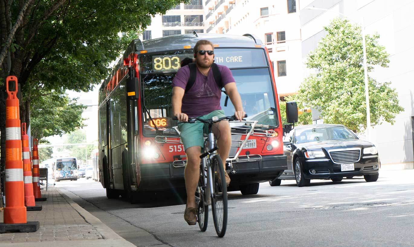 A man rides his bicycle next to a bus in downtown Austin, Texas.