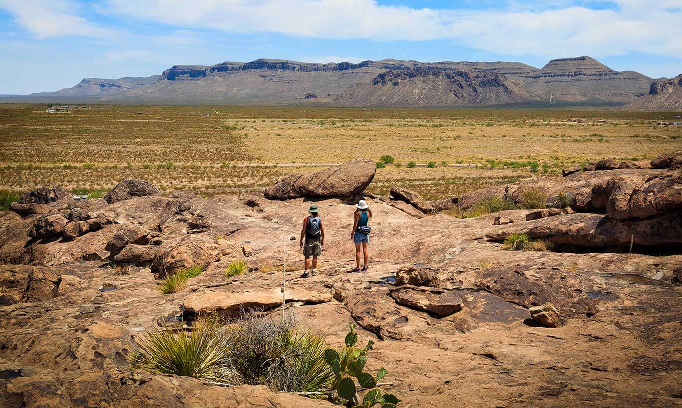 Two hikers gaze out at the desert landscape and huge mountains at Hueco Tanks State Park