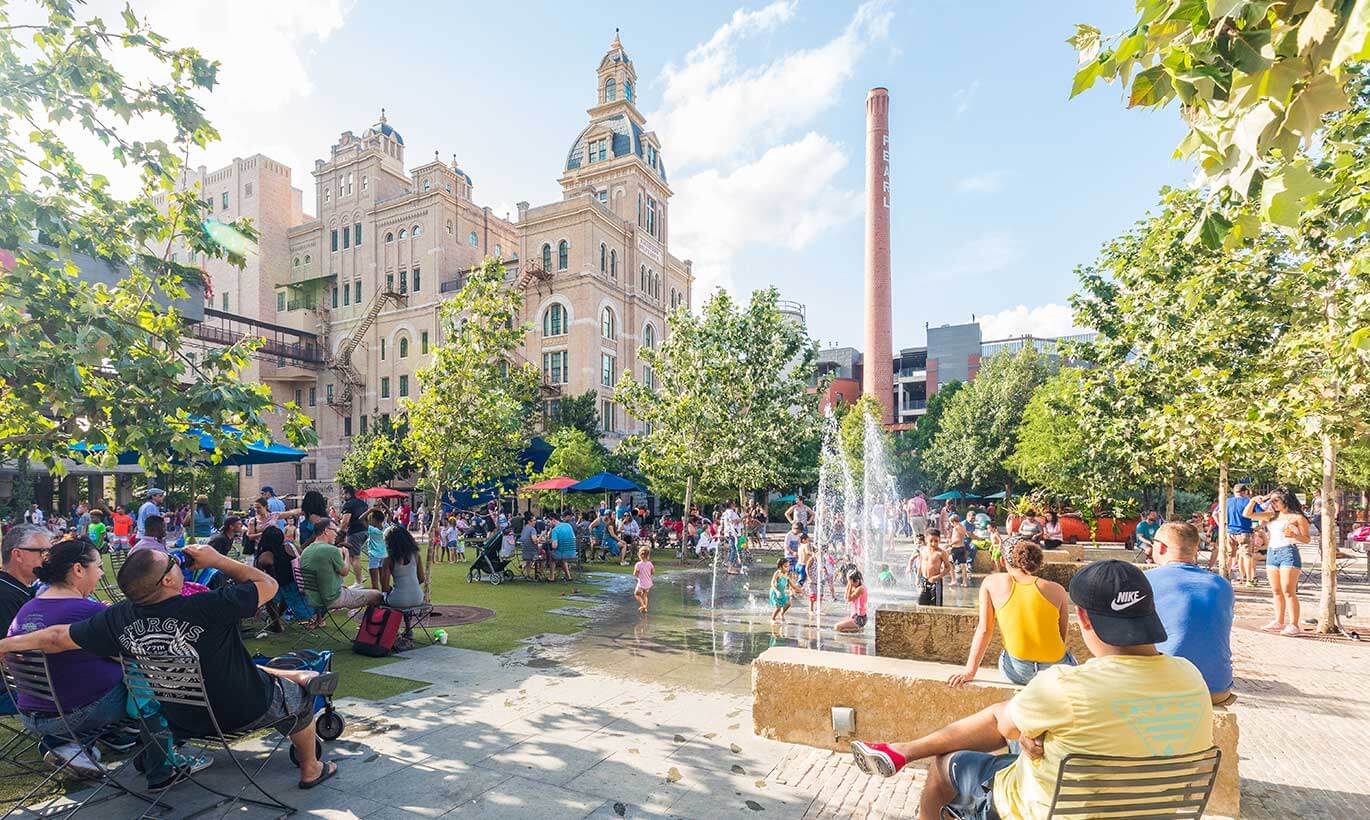 Groups of people gather in a courtyard and lawn space outside of Pearl Brewery in San Antonio, Texas